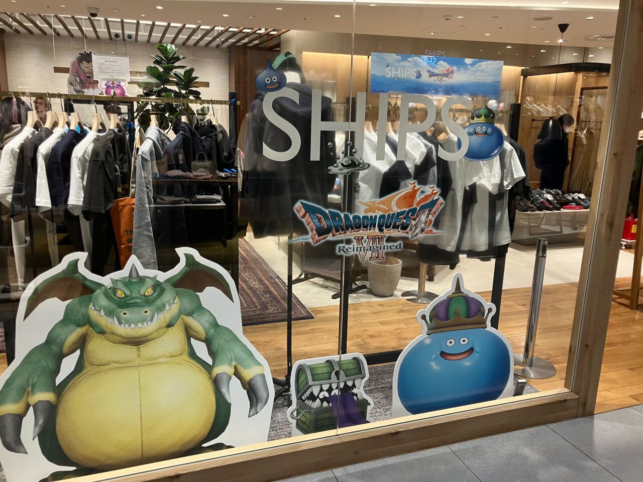 Storefront display with Dragon Quest characters and monsters (yellow dragon, blue slime, and others) on glass windows in a clothing store.